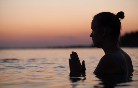 Woman in sea water at sunset alone. She praying or meditating